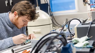 A Biomedical Signals and Systems student works on an electronic circuit in a lab filled with specialised equipment and cables.