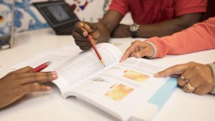 This image shows a close-up of people engaged in a research session or discussion, focusing on an open textbook with text and diagrams