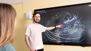 Two Computer Science students engage with a large interactive screen showing a digital map with interconnected lines and nodes.