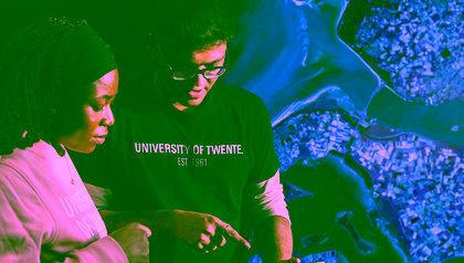 Two students examine a tablet together in front of a large satellite image, highlighting collaborative learning in geo‑information and earth observation