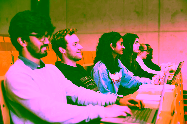 Six students sit in and lecture hall and listen