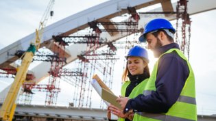 Two engineers with construction drawings at a bridge under construction