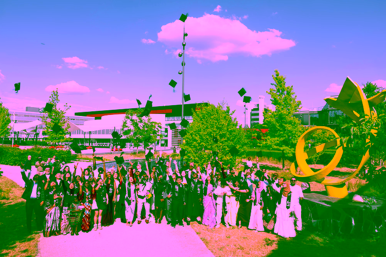Master’s graduates specialising in spatial data science celebrate outdoors in academic robes, with caps flying in front of a the distinctive yellow ITC sculpture near the Langezijds university building."