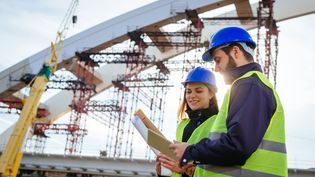 Two engineers with construction drawings at a bridge under construction