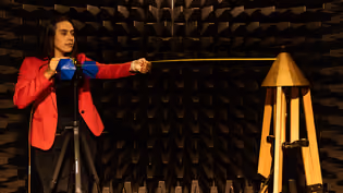 An Electrical Engineering student stands in an anechoic chamber, testing her project work.