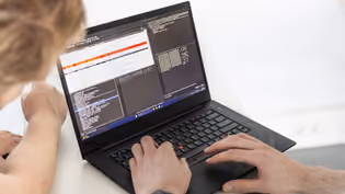 Two Computer Science students work on a laptop displaying code and data analysis.
