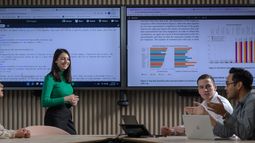 Four Business IT students collaborate in a meeting room with two large screens showing code and data visualisations.