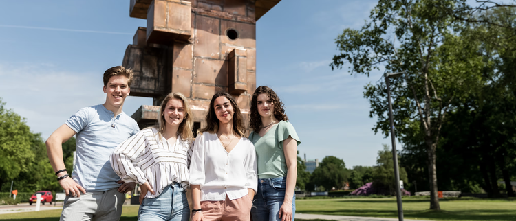 Vier Studierende posieren vor dem Kunstwerk Head auf dem Campus.