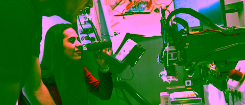 Electrical Engineering student examines a circuit board under a microscope, surrounded by lab equipment on a busy workspace
