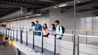 Een groep mensen staat op een binnenpasserelle en kijkt vanaf de railing uit over de open ruimte beneden.