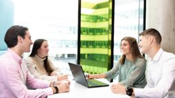 students at table talking and working on laptop