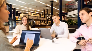 students at round table looking at one for presentation