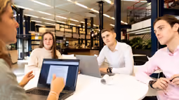 students at round table looking at one for presentation