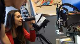 Electrical Engineering student uses a microscope while another observes, surrounded by lab equipment and a computer monitor.
