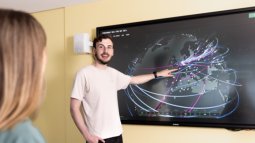 Two Computer Science students engage with a large interactive screen showing a digital map with interconnected lines and nodes.