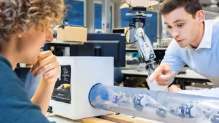 Students discuss a robotic arm in a transparent tube in the RAM lab at the University of Twente.