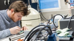 A Biomedical Signals and Systems student works on an electronic circuit in a lab filled with specialised equipment and cables.