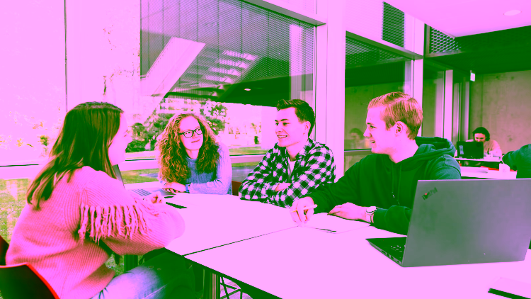 Four mathematics students are sitting together at a table in a modern study space, engaged in discussion.