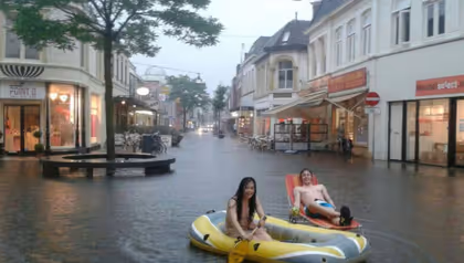 Two UT students in a small boat and on a deck chair in the flooded city centre of Enschede.