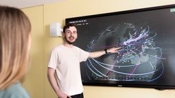Two Cyber Security students engage with a large interactive screen showing a digital map with interconnected lines and nodes.