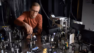 A student adjusts a photonics setup with lenses, mirrors, and optical components.